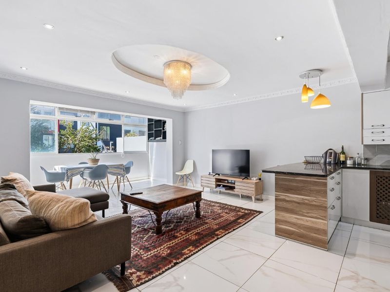 Spacious open-plan living and kitchen area featuring modern porcelain tiling, recessed lighting, a decorative ceiling feature, and a functional kitchen island with granite countertops.