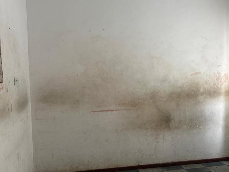 An empty bedroom featuring checkered floor tiles and walls requiring significant repair and repainting due to extensive surface staining.