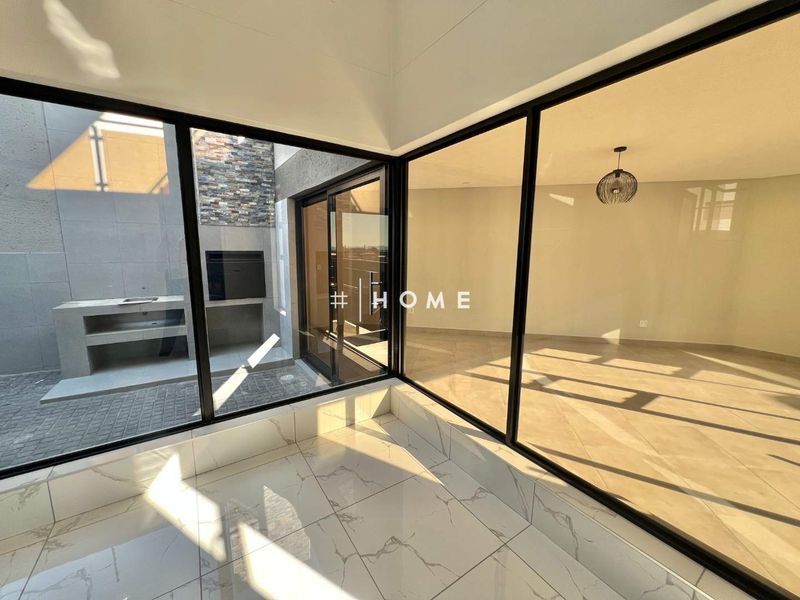Bright open plan living area featuring large format porcelain tiles, expansive black aluminium windows, and a seamless transition to an outdoor built-in braai area.