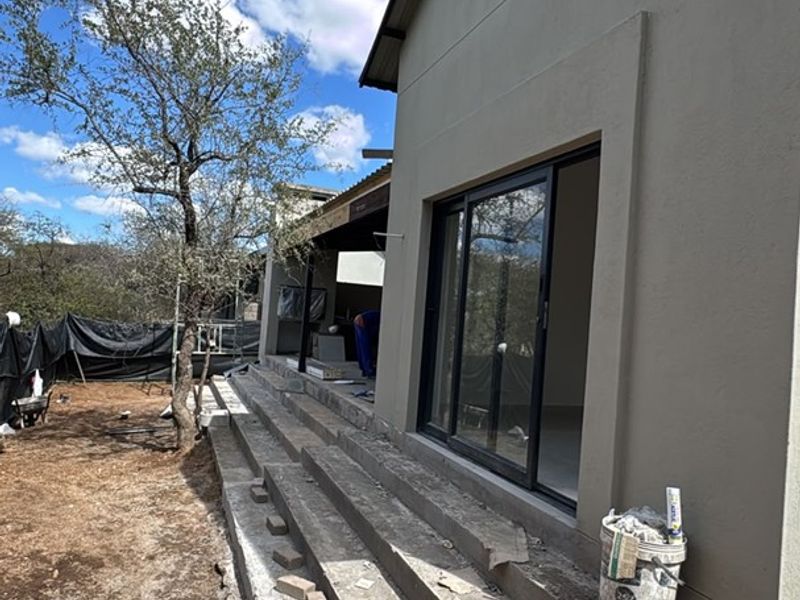 Rear exterior view of the property featuring sliding glass doors and unfinished concrete steps leading to the garden area.