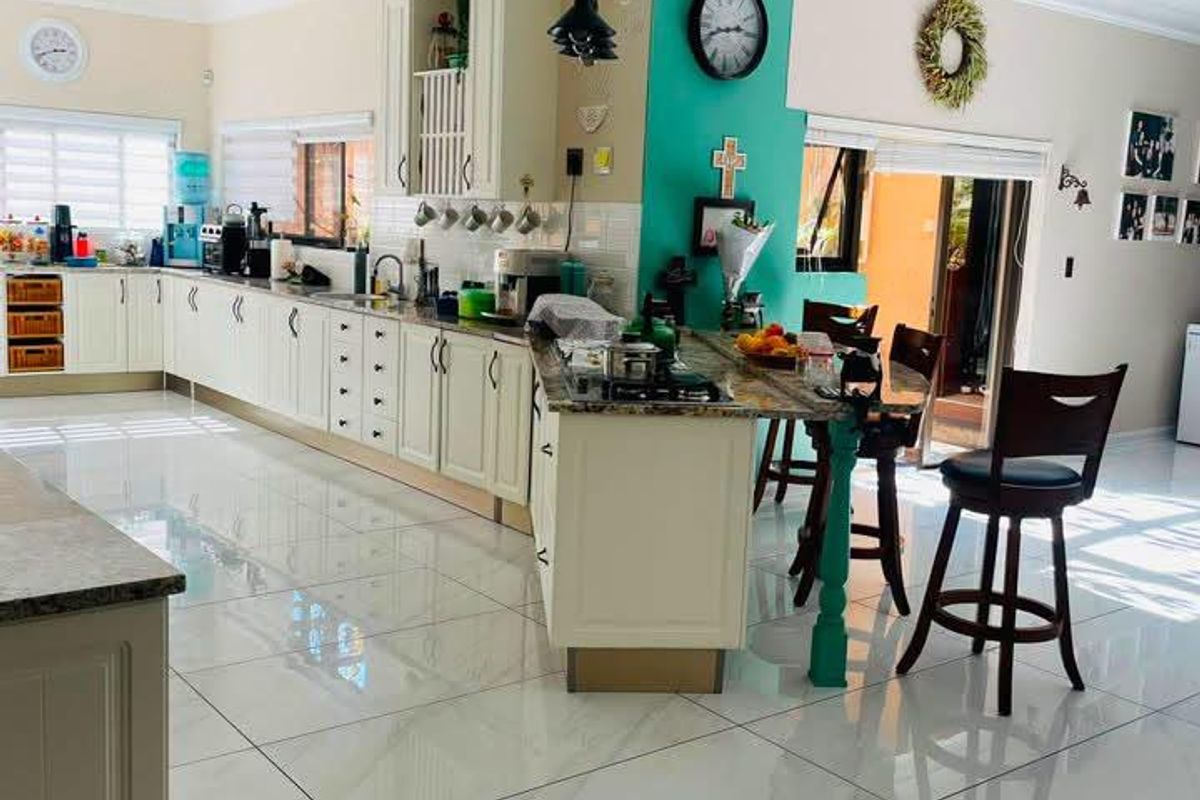 Spacious kitchen featuring extensive cabinetry, granite countertops, a central island with a cooktop, and polished tile flooring with natural light.