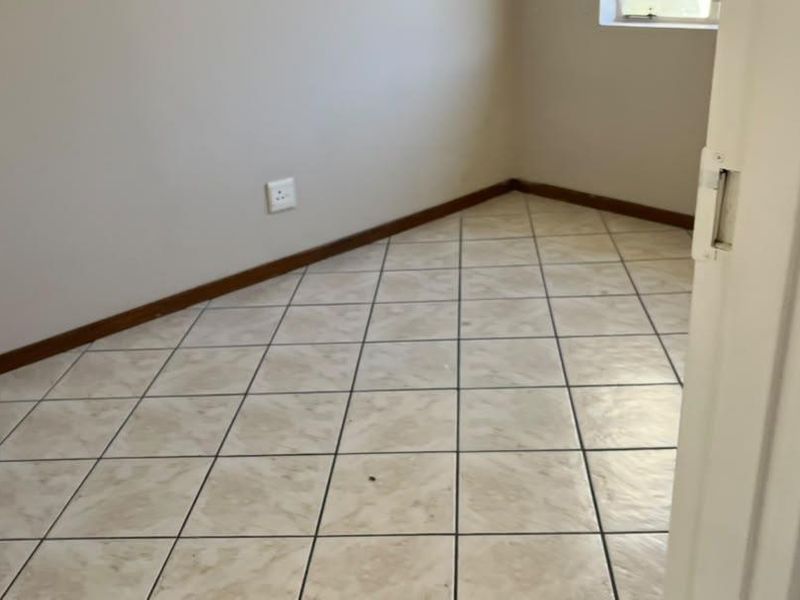 An empty bedroom featuring neutral wall paint, tiled flooring, and a window, providing a blank canvas for personalization.