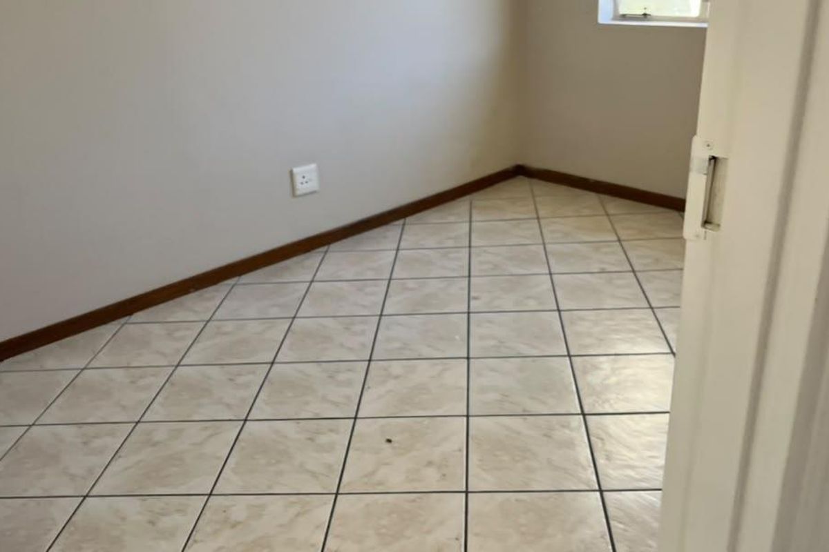 An empty bedroom featuring neutral wall paint, tiled flooring, and a window, providing a blank canvas for personalization.