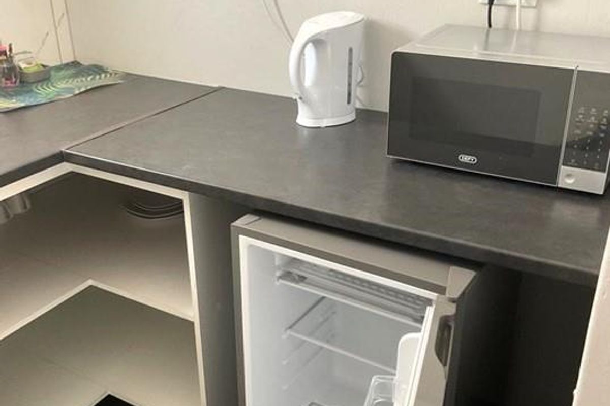 A compact kitchenette area featuring laminate countertops, open shelving, and space for a small under-counter refrigerator.