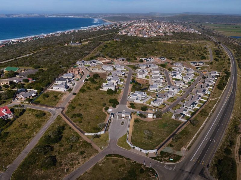 Aerial view of a residential estate development featuring a gated entrance, internal road network, and proximity to the coastline.