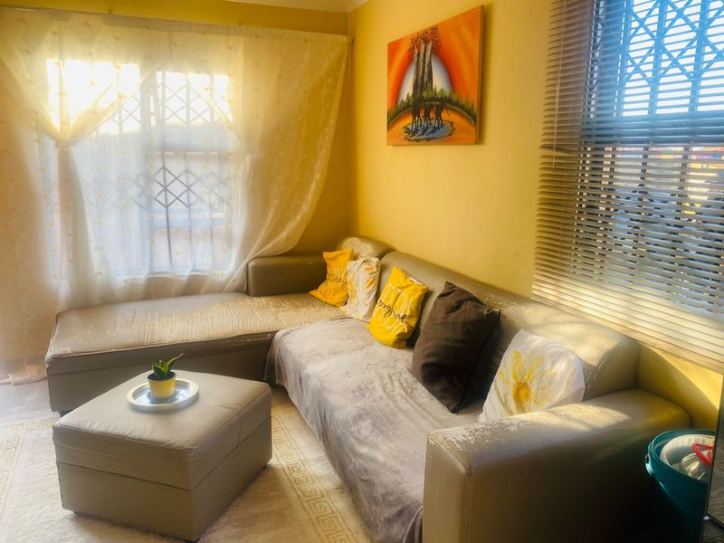 A living room featuring natural light through windows with security bars and venetian blinds, providing a functional space for relaxation.