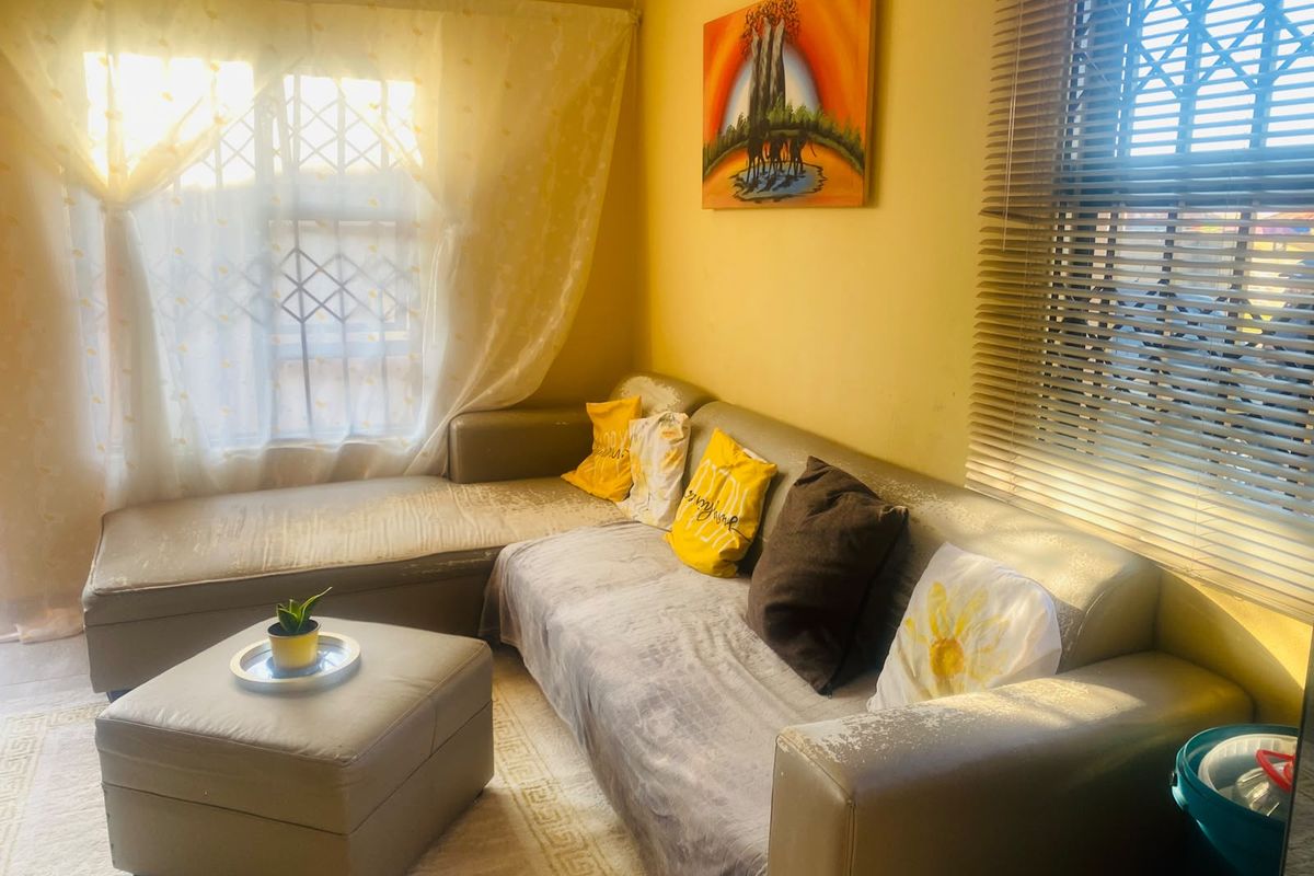 A living room featuring natural light through windows with security bars and venetian blinds, providing a functional space for relaxation.