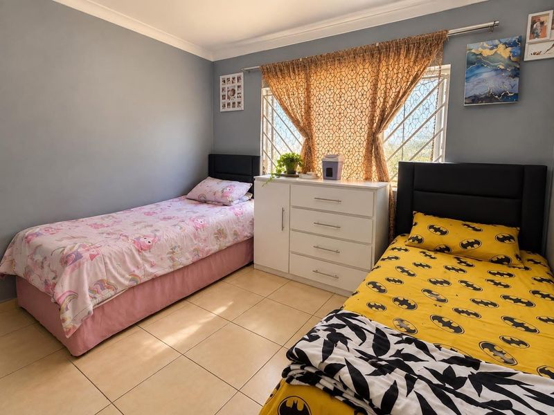 A functional bedroom featuring tiled flooring, security bars on the window, and neutral wall finishes.