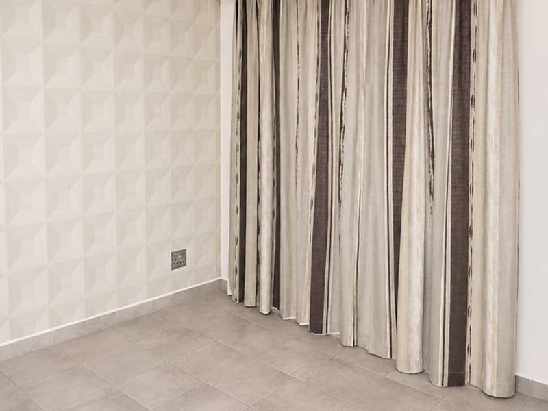 A clean, empty bedroom featuring neutral ceramic floor tiles, a textured feature wall, and a modern pendant light fixture.