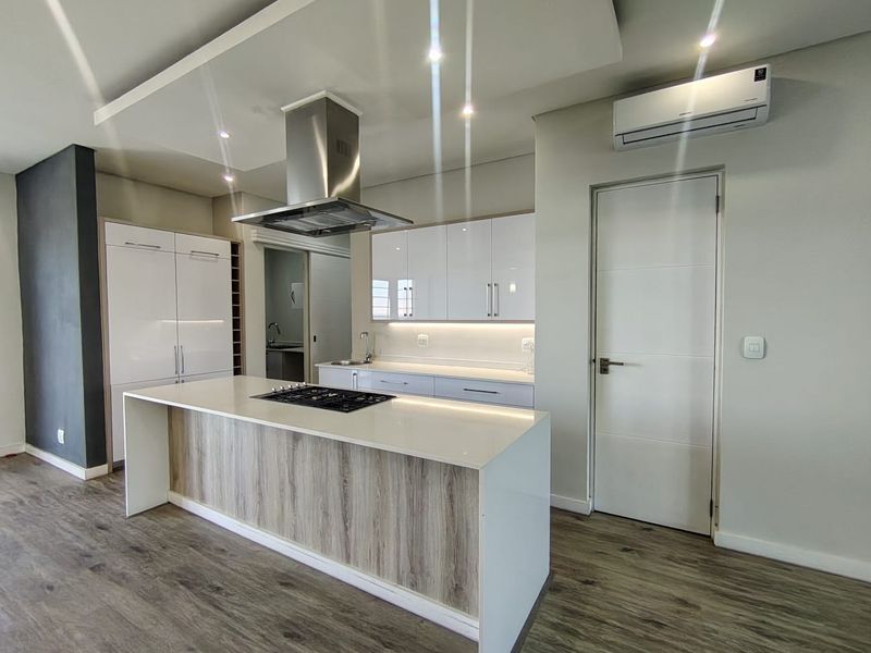 Modern kitchen featuring a central island with gas cooktop, sleek white cabinetry, stone countertops, and integrated lighting in a contemporary open-plan setting.