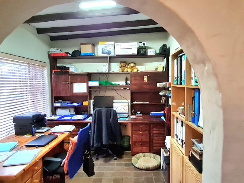 A home office featuring built-in wooden cabinetry, shelving, exposed ceiling beams, and an arched entryway.