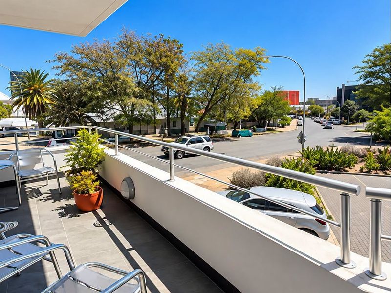 A modern, well-maintained balcony featuring tiled flooring and a sleek metal railing, offering an elevated view of the surrounding street and neighborhood.