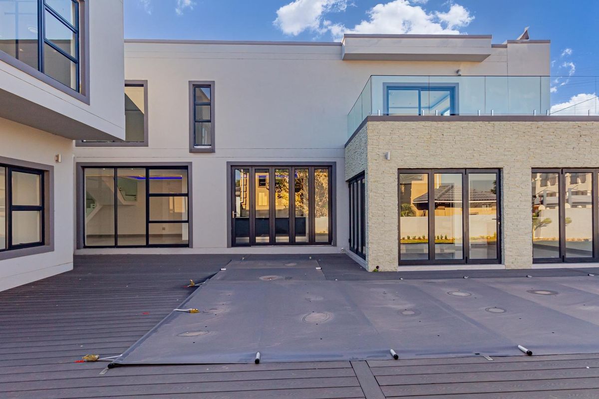 Modern rear exterior view featuring a spacious timber deck, large glass sliding doors, and a glass-balustrade balcony on the upper level.