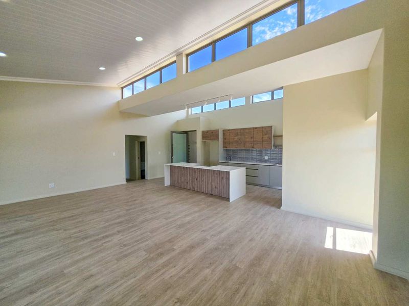 Spacious open-plan living area featuring high ceilings, clerestory windows for natural light, and a modern kitchen with a central island and contemporary cabinetry.