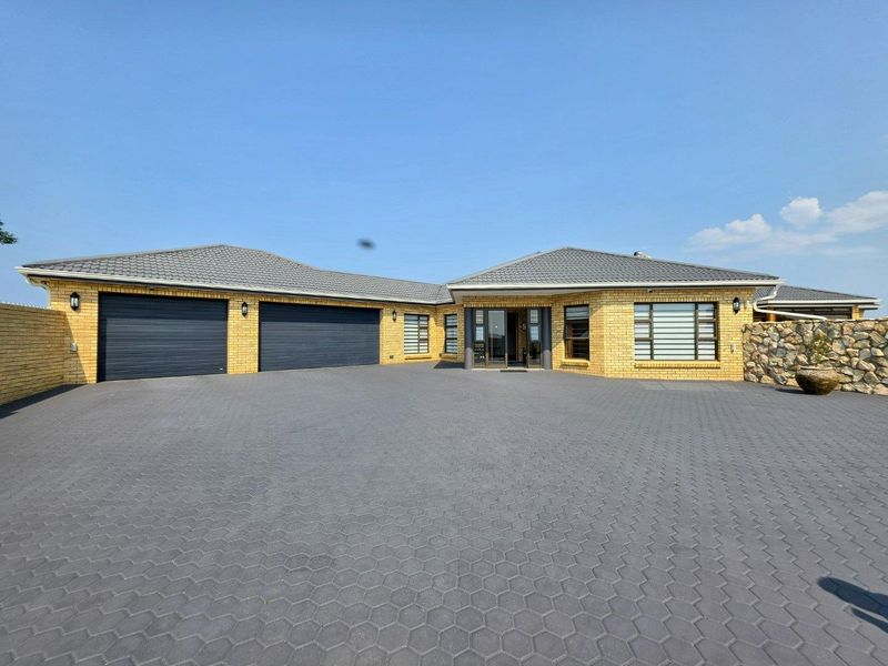 Front elevation of a modern brick house featuring a spacious paved driveway, double garage, and stone-clad accents under a tiled roof.