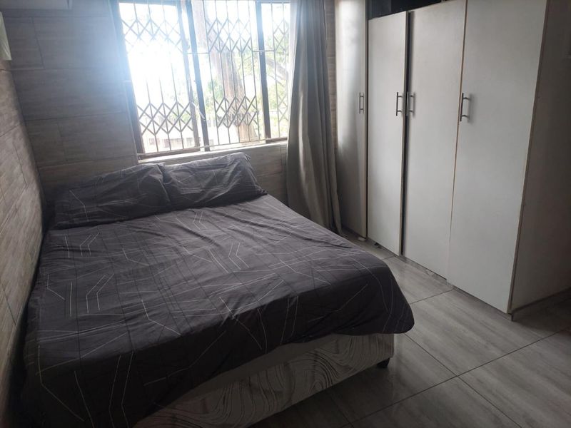 A bedroom featuring tiled flooring, built-in cupboards, and a window with a security gate.