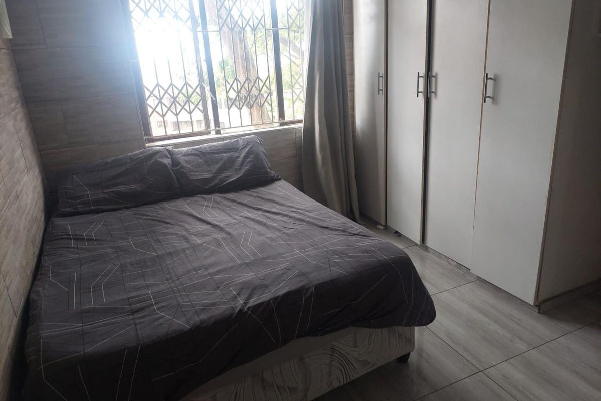 A bedroom featuring tiled flooring, built-in cupboards, and a window with a security gate.