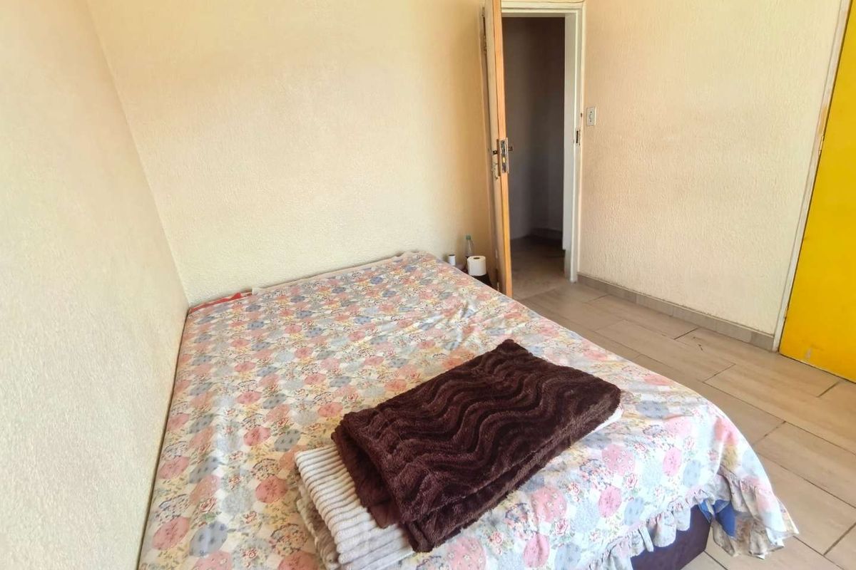 A simple bedroom featuring tiled flooring and neutral wall finishes, providing a functional space with direct access to an adjoining room.