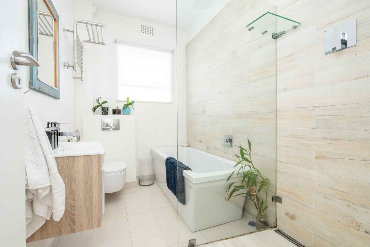 Modern bathroom featuring a wall-mounted vanity, a sleek bathtub, and a glass-enclosed shower area with light-toned wall tiling.