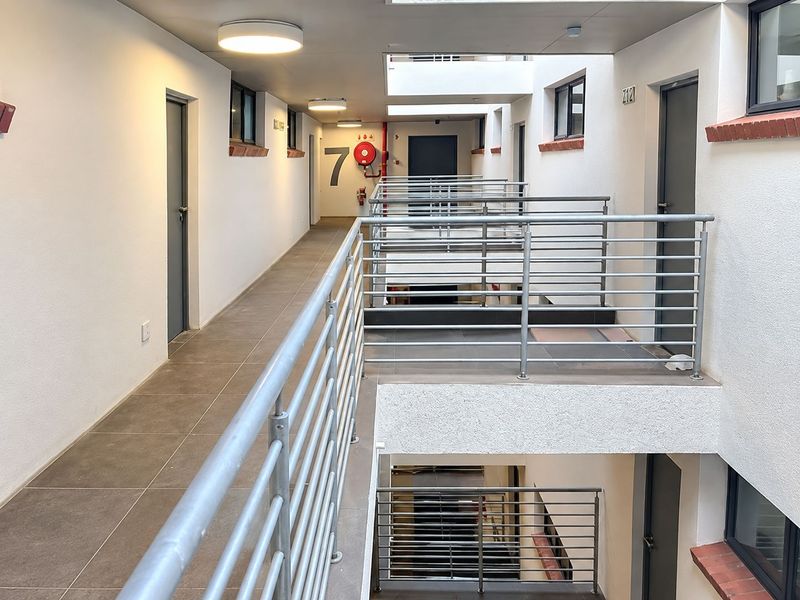 A clean and well-maintained apartment building hallway featuring tiled floors, metal safety railings, and access to multiple residential units.