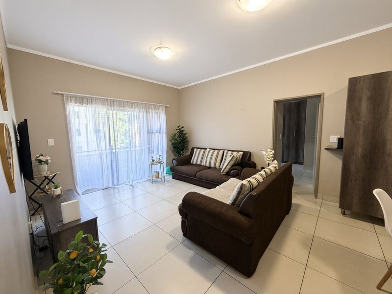 A well-maintained living room featuring neutral tiled flooring, ample natural light from a sliding glass door, and a clean, functional layout.