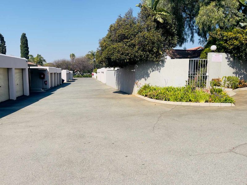 Exterior view of the apartment complex driveway featuring a row of garages, perimeter wall, and security access gate.