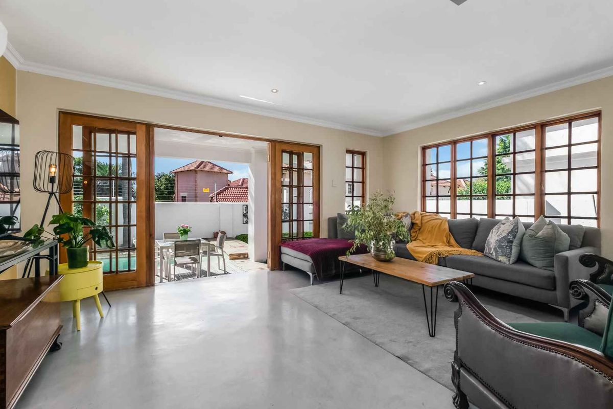 Spacious living room featuring polished concrete floors, large timber-framed windows, and double doors opening onto a patio area.