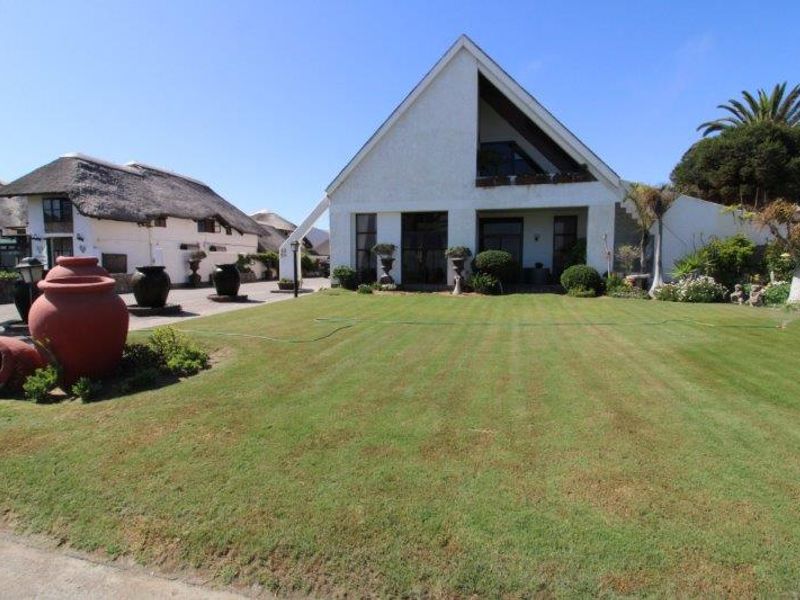 Front view of a property featuring a large lawn, landscaped garden, and a distinctive pitched roof design.