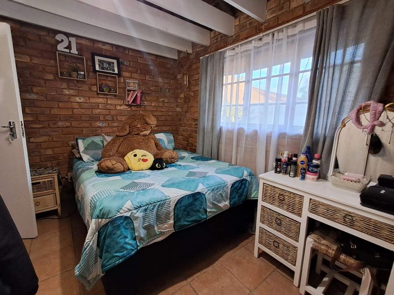 A cozy bedroom featuring rustic exposed brick walls, exposed ceiling beams, and tiled flooring, creating a warm and characterful living space.