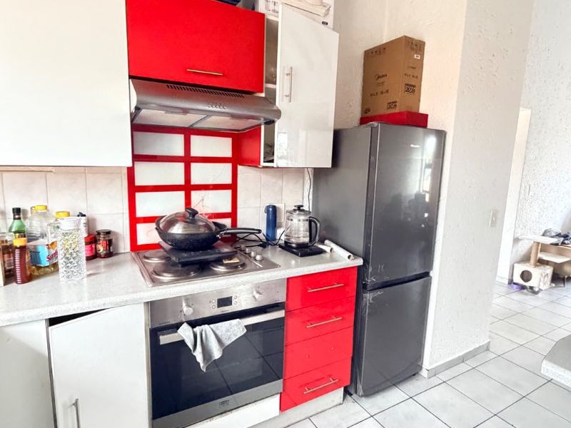 A functional kitchen featuring red and white cabinetry, a built-in oven with gas hob, extractor fan, and tiled flooring.