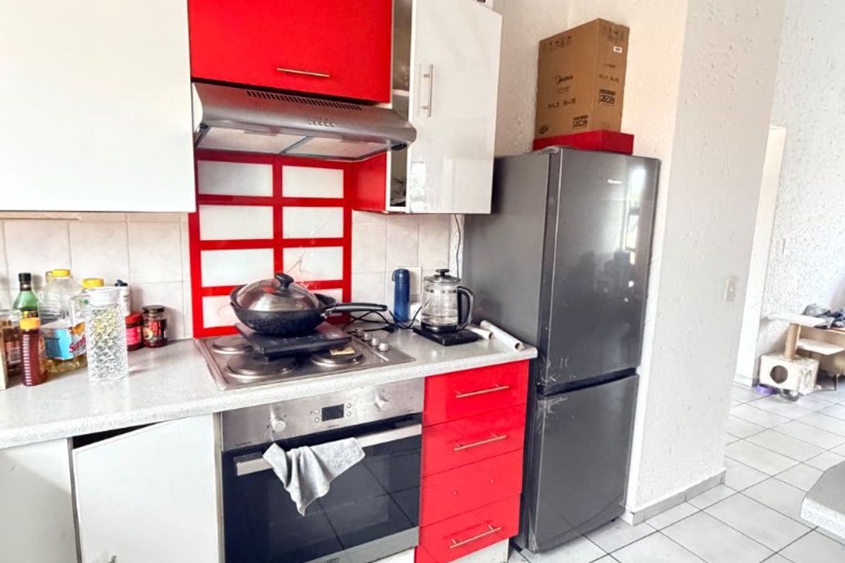 A functional kitchen featuring red and white cabinetry, a built-in oven with gas hob, extractor fan, and tiled flooring.