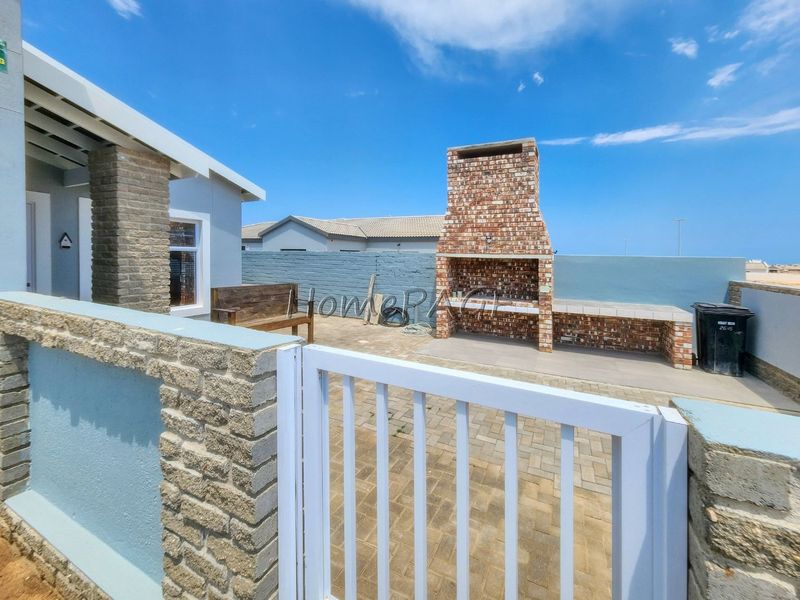 Outdoor patio area featuring a built-in brick braai, paved flooring, and secure boundary walling with a metal gate.