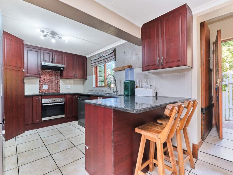 A functional kitchen featuring dark wood cabinetry, granite countertops, a breakfast bar, and a mosaic tile backsplash with built-in oven and hob.