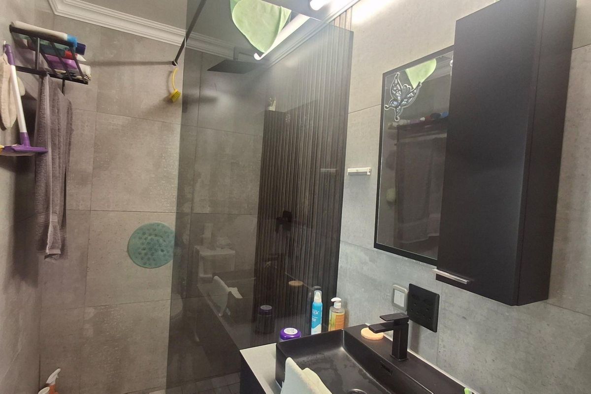 Modern bathroom featuring a walk-in shower with glass screen, dark vanity cabinet with vessel sink, and contemporary grey wall tiling.