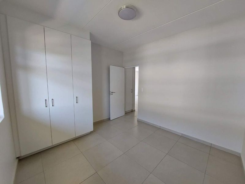 A clean, empty bedroom featuring neutral tiled flooring and white built-in cupboards, offering a bright and versatile space ready for personalization.
