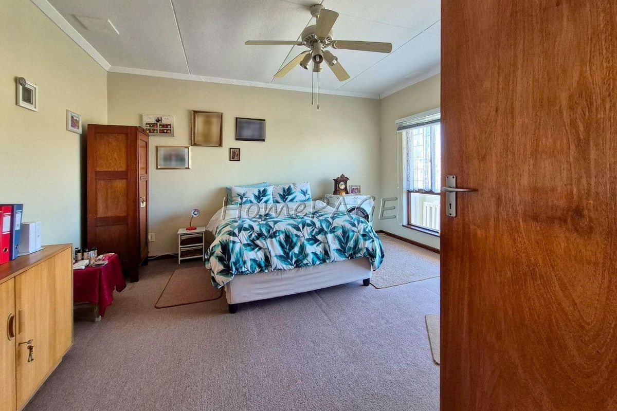 A spacious bedroom featuring neutral wall tones, a ceiling fan, and large windows allowing for natural light.