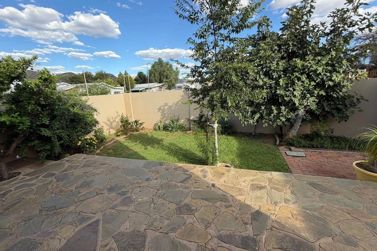 A private rear garden featuring a natural stone paved patio, a small lawn area, and perimeter boundary walls.