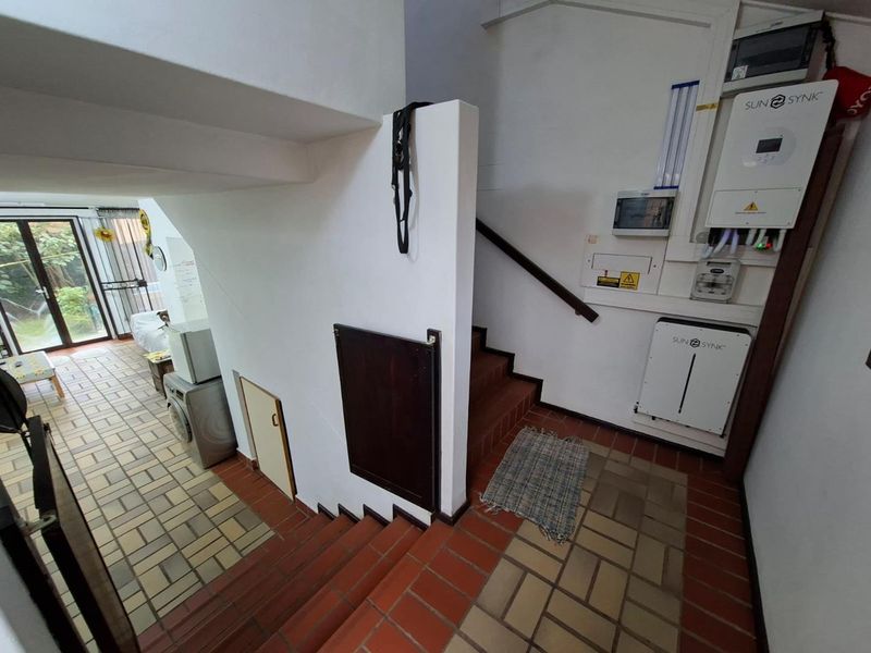 A functional hallway area featuring a staircase, tiled flooring, and a wall-mounted solar inverter and battery storage system.