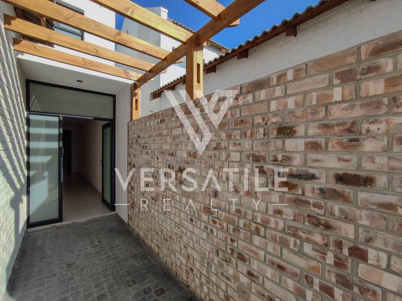 A modern outdoor patio area featuring a timber pergola, exposed brick wall, and paved flooring, providing a seamless transition to the interior living space.