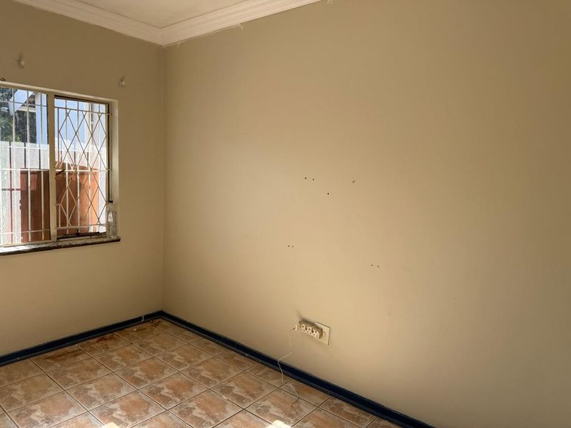 An empty bedroom featuring tiled flooring, security bars on the window, and neutral wall finishes requiring minor cosmetic repairs.