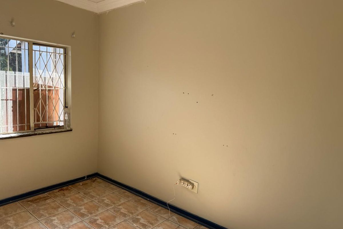 An empty bedroom featuring tiled flooring, security bars on the window, and neutral wall finishes requiring minor cosmetic repairs.