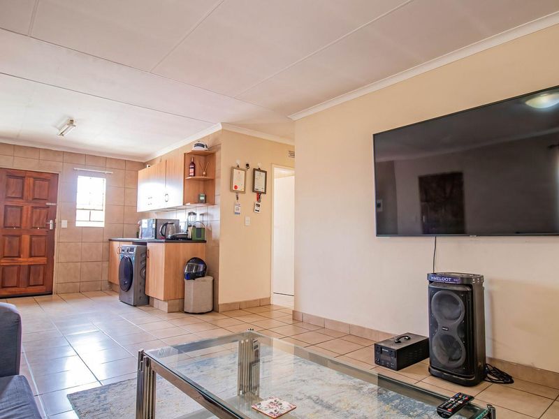 Open-plan living area featuring tiled flooring and a compact kitchen with built-in cabinetry, seamlessly connecting the lounge and cooking space.