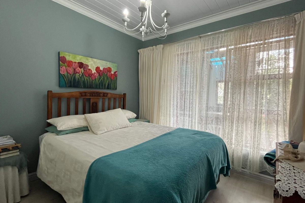 A well-maintained bedroom featuring crown molding, a classic chandelier, and large windows with sheer curtains allowing for natural light.