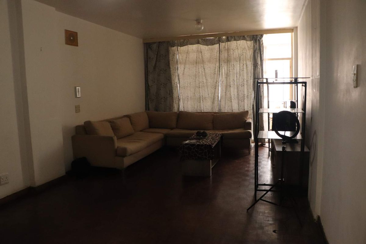 A dimly lit living room featuring parquet flooring and large windows with curtains, offering a blank canvas for potential interior updates.