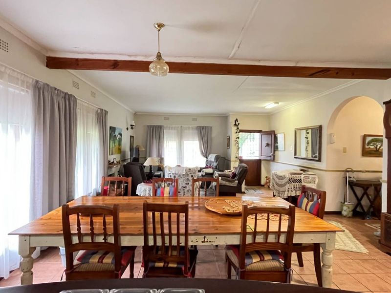 Spacious open-plan living and dining area featuring tiled floors, an exposed timber ceiling beam, and a classic arched entryway.