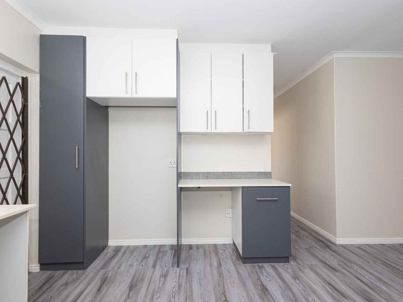 A clean, modern kitchen area featuring two-tone cabinetry, light grey laminate flooring, and a built-in workspace or prep area.