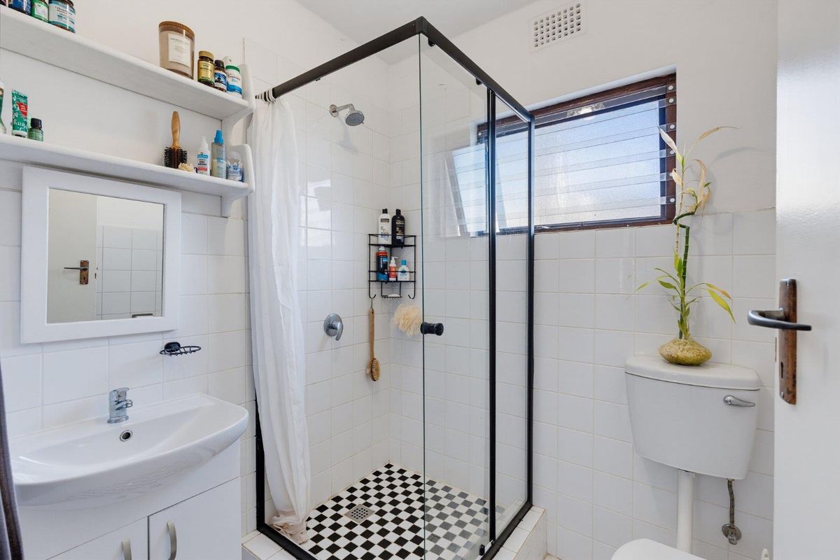 A functional bathroom featuring a glass-enclosed shower, wall-mounted basin with vanity storage, and a standard toilet with white tiled finishes.