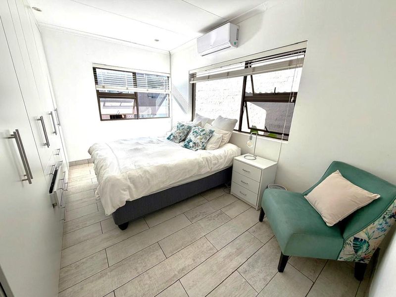 A bright bedroom featuring built-in floor-to-ceiling wardrobes, tiled flooring, and a wall-mounted air conditioning unit.