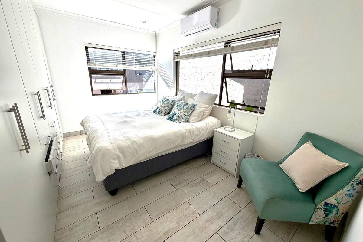 A bright bedroom featuring built-in floor-to-ceiling wardrobes, tiled flooring, and a wall-mounted air conditioning unit.