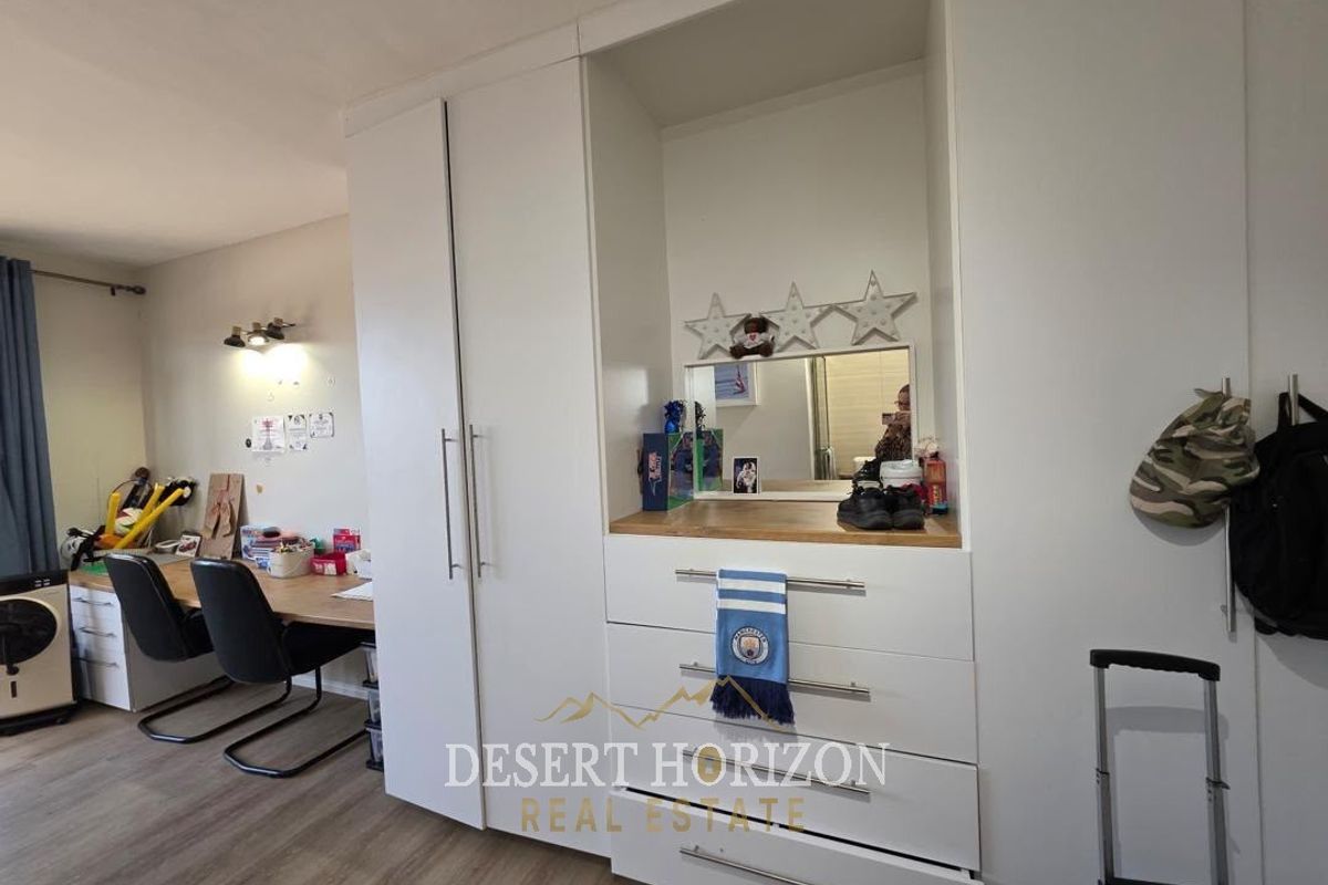 Bedroom featuring a large white built-in wardrobe with an integrated vanity station and modern laminate flooring.